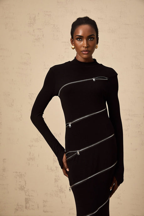 A woman wearing a black fitted maxi dress with zipper details standing against a plain background