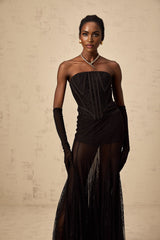 A woman wearing a black floral lace corset matching skirt and gloves set with delicate lace patterns and a fitted silhouette