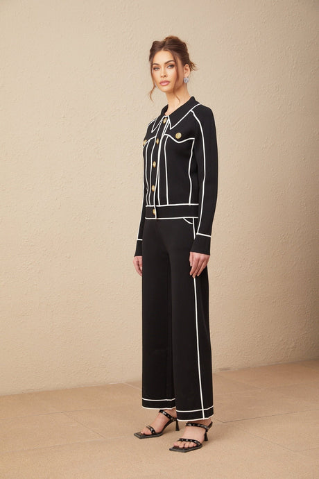 A woman wearing a black jacket and matching trousers both with white piped trim The set has a sleek professional appearance