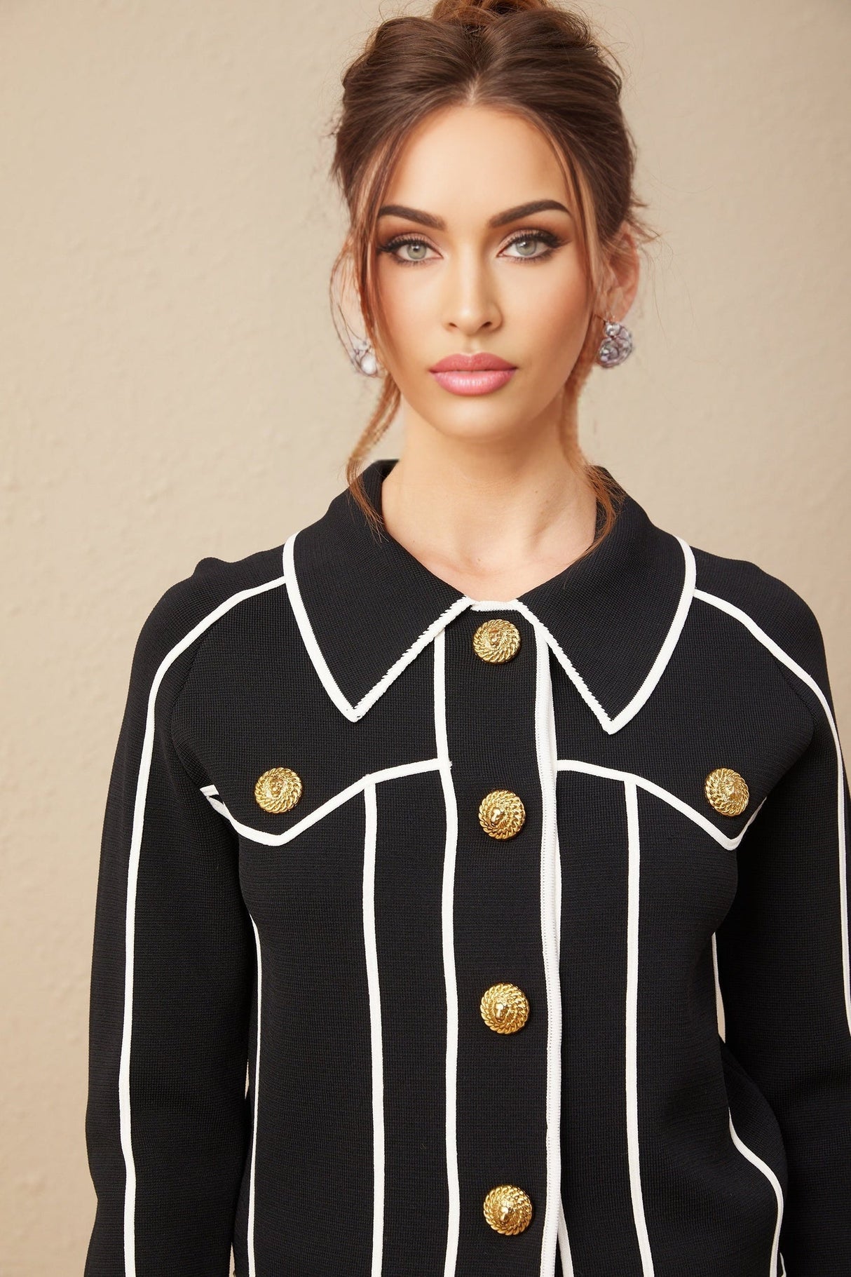 A woman wearing a black jacket and matching trousers with white piping trim The jacket has a tailored fit and the trousers are slim cut creating a sleek coordinated outfit