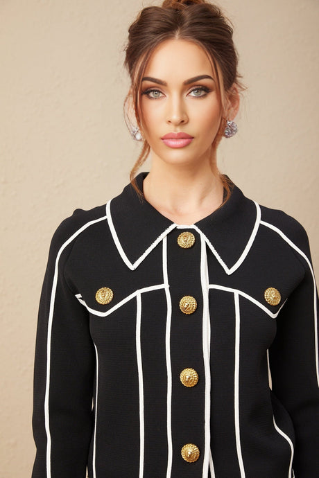 A woman wearing a black jacket and matching trousers with white piping trim The jacket has a tailored fit and the trousers are slim cut creating a sleek coordinated outfit