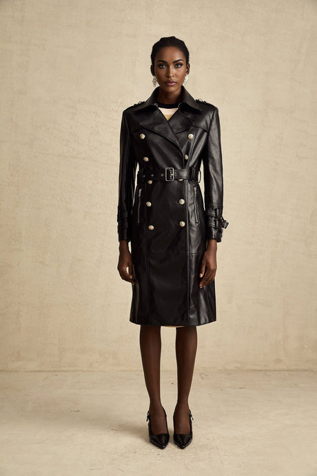 A woman wearing a black leather coat with double breasted buttons and a belt at the waist the coat has a sleek design and falls to about knee length