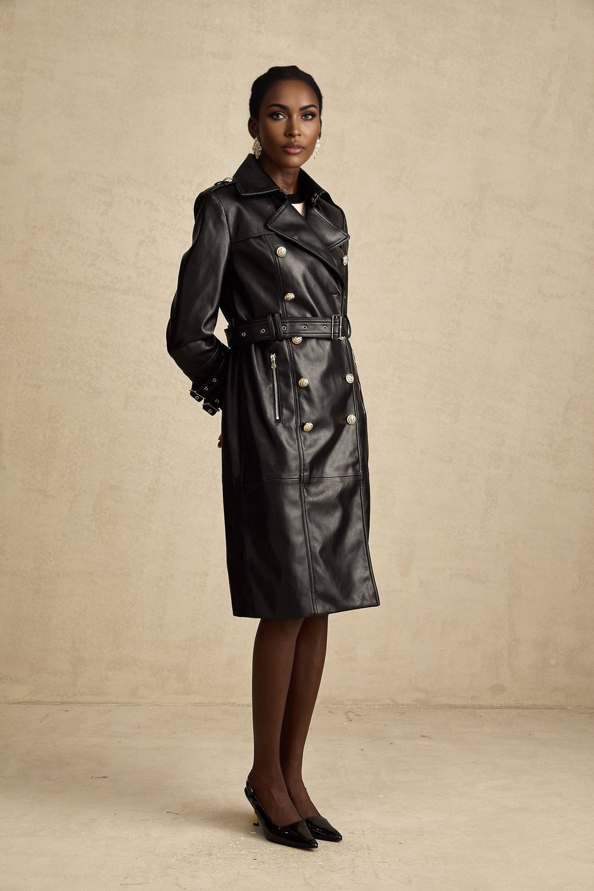 A woman wearing a black leather coat with double breasted buttons and a belt at the waist
