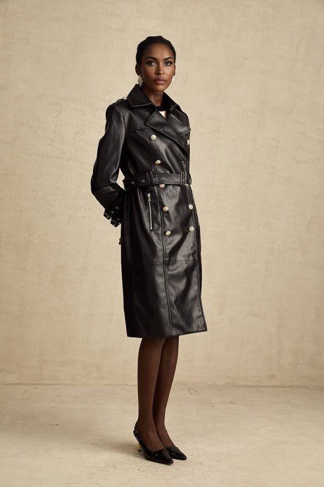 A woman wearing a black leather coat with double breasted buttons and a belt at the waist