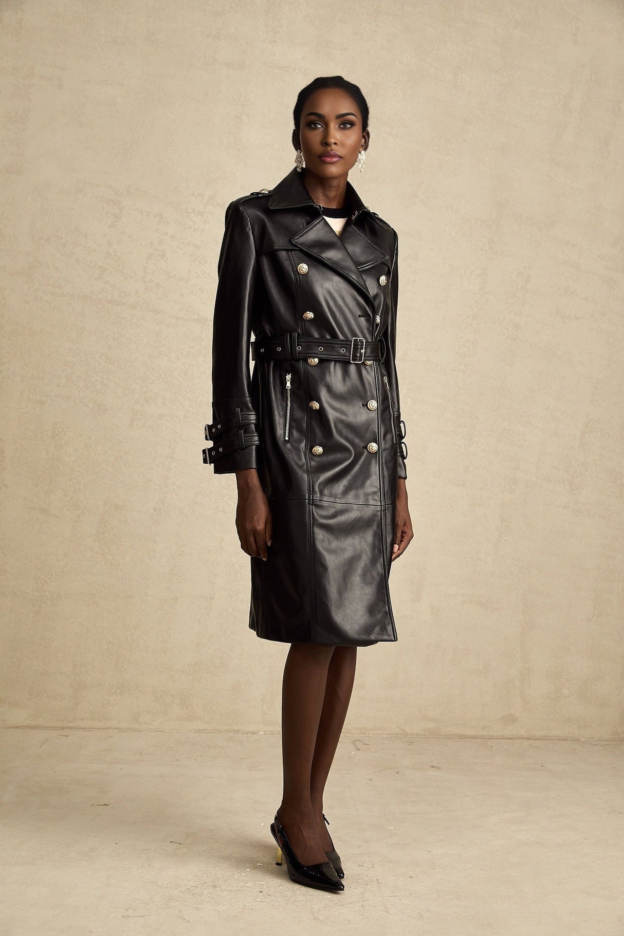 A woman wearing a black leather coat with double breasted front buttons and a belt cinched at the waist