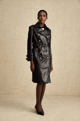 A woman wearing a black leather coat with double breasted front buttons and a belt cinched at the waist
