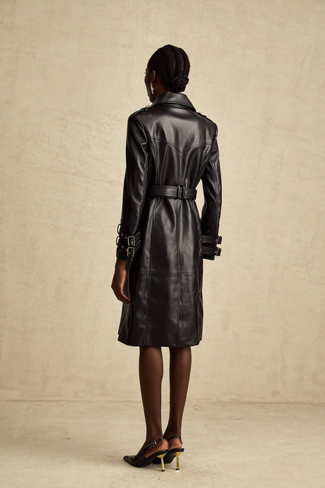A woman wearing a black leather coat with doublebreasted front closure and a belt at the waist