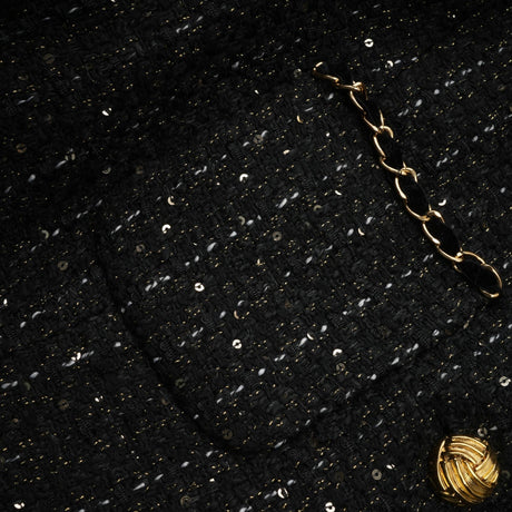 A woman wearing a black mini dress featuring a combination of tweed fabric and sequin panels The dress has a classic silhouette with short sleeves and a high neckline showcasing the contrast between the textured tweed and shimmering sequins