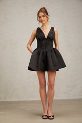 A woman wearing a black mini dress with a Vneck and flared skirt standing in a neutral background