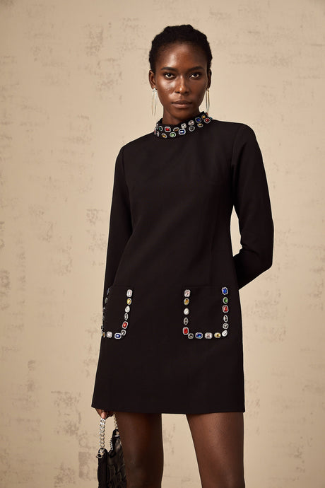 A woman wearing a black mini dress with long sleeves adorned with crystal embellishments