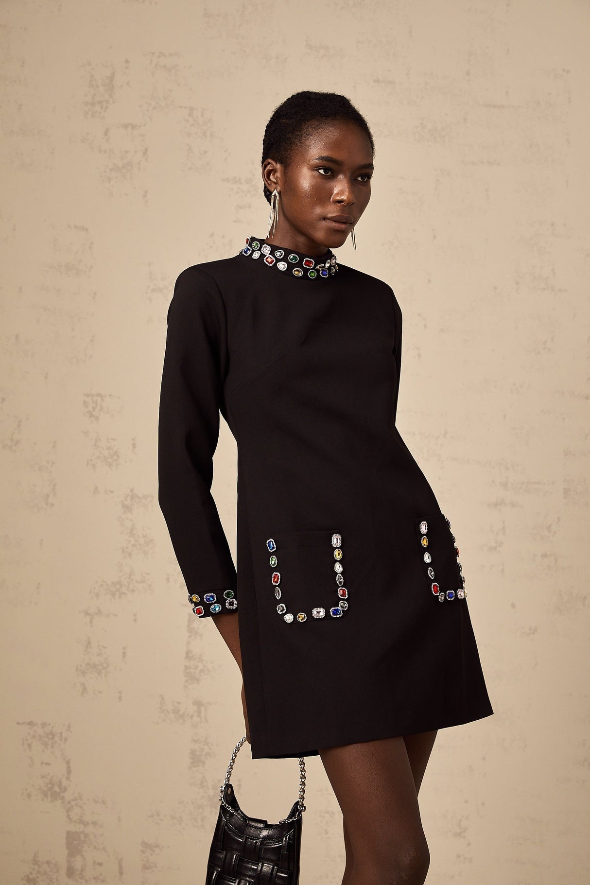 A woman wearing a black mini dress with long sleeves and crystal embellishments standing in a neutral pose