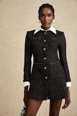 A woman wearing a black mini dress with tweed fabric and sequin panels named Audrey standing in a stylish pose