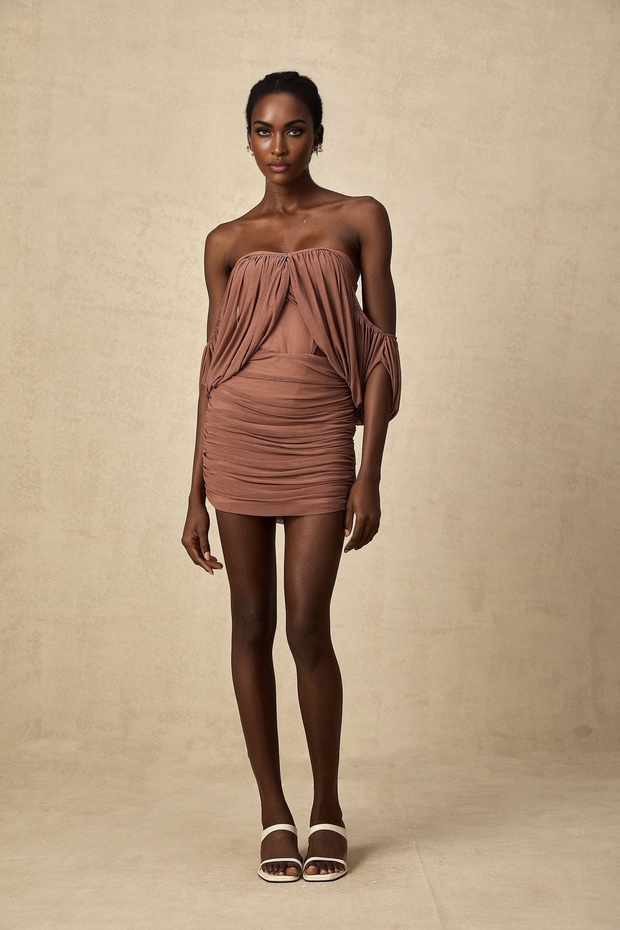 A woman wearing a black offshoulder bodysuit paired with a matching black skirt standing in a neutral pose