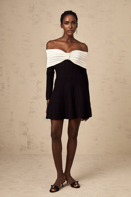 A woman wearing a black offshoulder mini dress with a bow detail and knit fabric