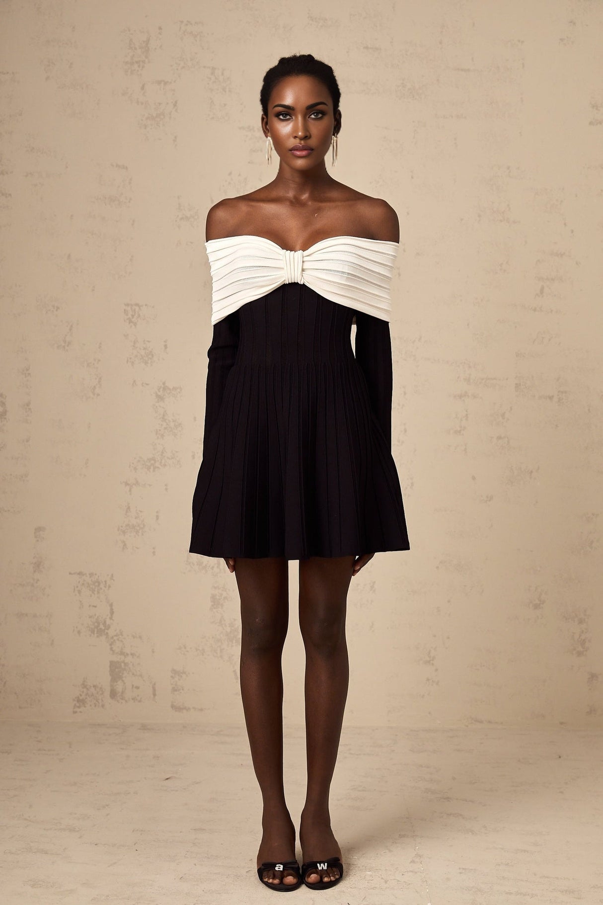 A woman wearing a black offshoulder mini dress with a bow detail and knit fabric