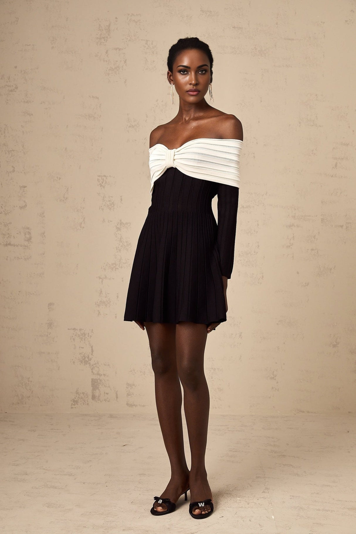 A woman wearing a black offshoulder mini dress with a bow detail on the neckline and a knitted fabric texture