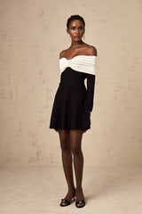 A woman wearing a black offshoulder mini dress with a bow detail on the neckline and a knitted fabric texture