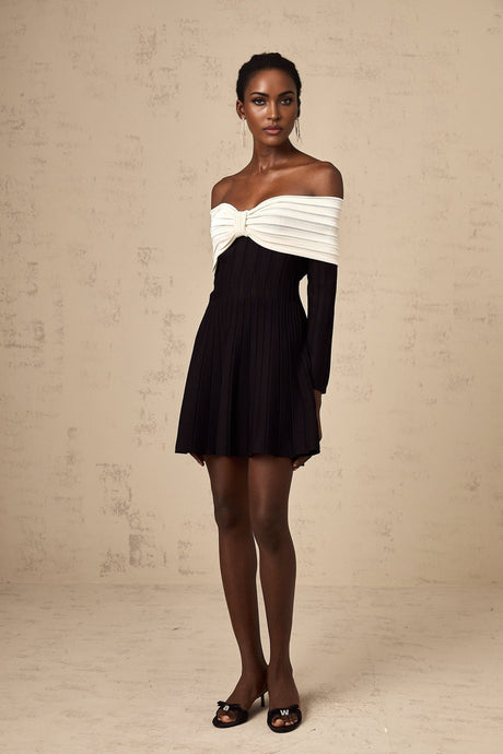 A woman wearing a black offshoulder mini dress with a bow detail on the neckline and a knitted fabric texture
