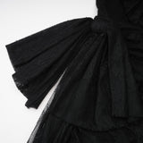 A woman wearing a black oneshoulder maxi dress with a cutout detail standing against a plain background
