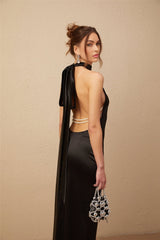 A woman wearing a black satin maxi dress with a halterneck design and faux pearl embellishments