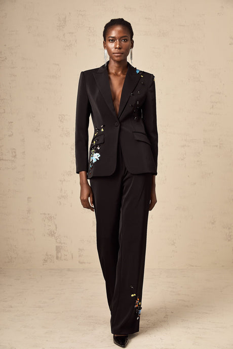 A woman wearing a black sequined blazer and matching trousers standing confidently against a plain background