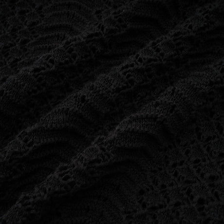 A woman wearing a black sequined matching set consisting of a crochet knit cardigan and skirt