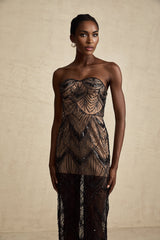 A woman wearing a black sequinned corset maxi dress with mesh details standing against a plain background