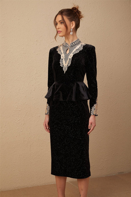 A woman wearing a black velvet midi dress with embellishments standing in a neutral pose against a plain background