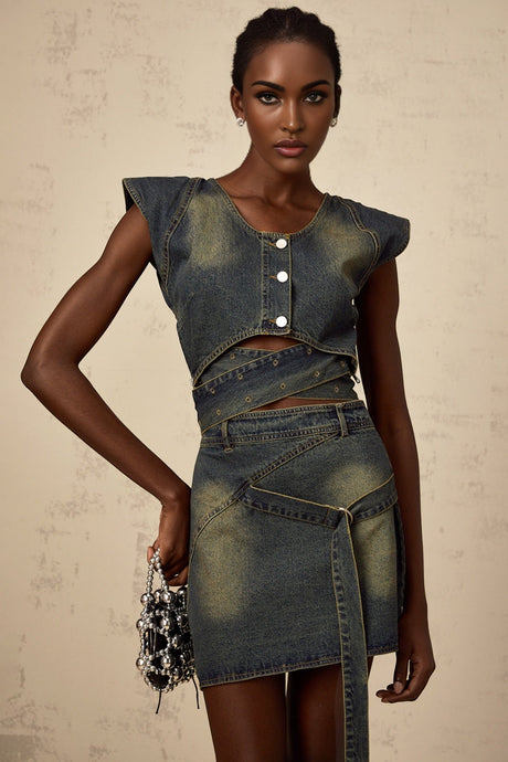 A woman wearing a blue denim matching set consisting of a crossover top and skirt The top has short sleeves and wraps across the chest while the skirt falls to mid thigh creating a coordinated outfit