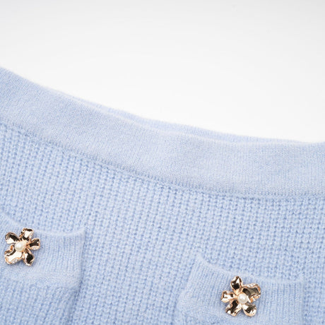 A woman wearing a blue knit matching set consisting of a blouse and skirt standing against a plain background