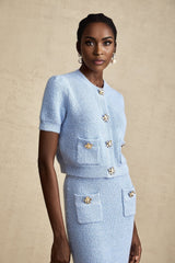 A woman wearing a blue knit matching set consisting of a blouse and skirt standing against a plain background