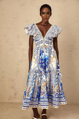 A woman wearing a blue midi dress with a baroque print pattern and tiered skirt design