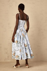 A woman wearing a blue midi dress with a floral print pattern standing against a plain background