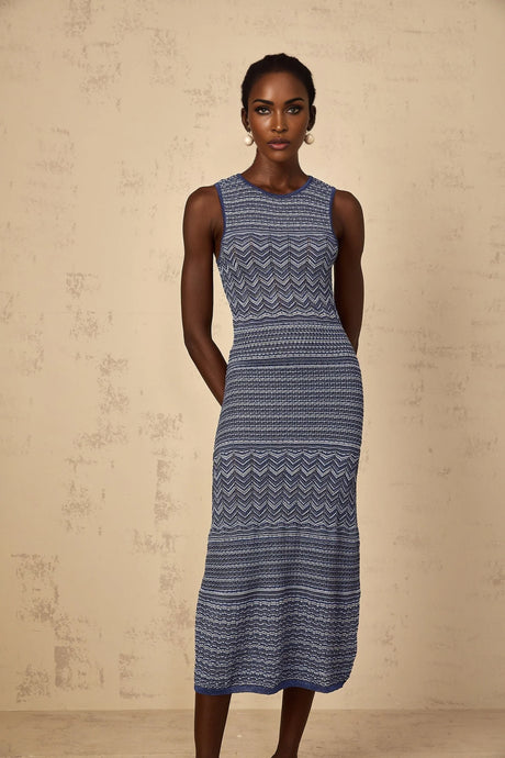 A woman wearing a blue midi dress with a wavy crochet knit pattern standing against a plain background