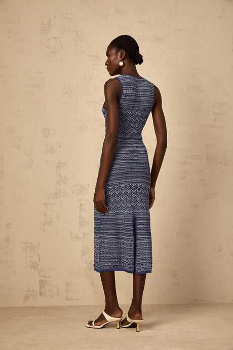 A woman wearing a blue midi dress with a wavy crochet knit pattern standing in a relaxed pose