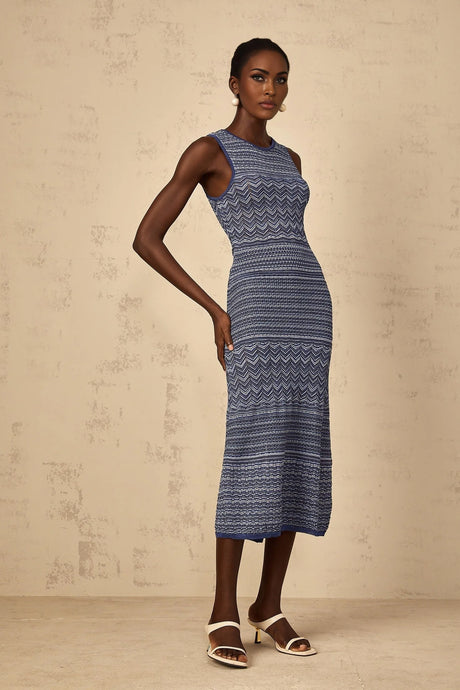A woman wearing a blue midi dress with a wavy crochet knit pattern standing in a relaxed pose