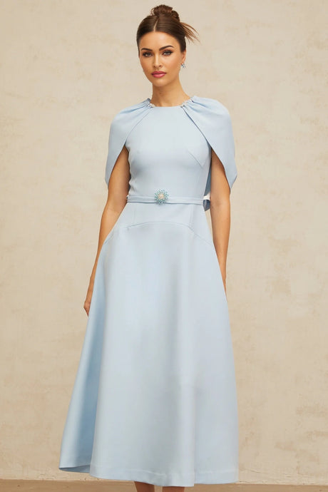 A woman wearing a blue midi dress with shawllike panels and embellishments standing in a neutral setting