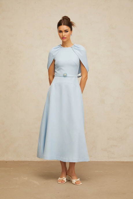 A woman wearing a blue midi dress with shawlstyle panel and embellished details standing in a neutral background