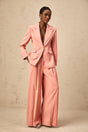 A woman wearing a bright pink matching set consisting of a blazer with cutout details and embroidery paired with coordinating trousers