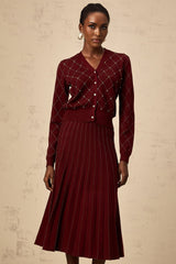 A woman wearing a bright red matching set consisting of a cardigan and skirt The cardigan features an argyle pattern with embellishments and the skirt is knitted in a coordinating style Both pieces have intarsia knit detailing The outfit is styled as a fashionable two piece ensemble
