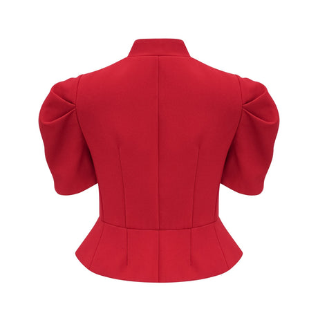 A woman wearing a bright red matching set consisting of a pleated blouse and skirt The blouse has long sleeves and a high neckline while the skirt falls to midi length with pleats throughout The outfit creates a stylish and coordinated look