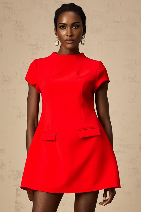 A woman wearing a bright red mini dress with cap sleeves standing against a plain background