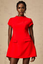 A woman wearing a bright red mini dress with cap sleeves standing against a plain background