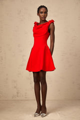 A woman wearing a bright red sleeveless mini dress with faux flower details standing against a plain background