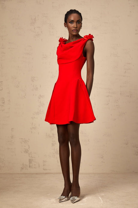 A woman wearing a bright red sleeveless mini dress with faux flower details standing against a plain background