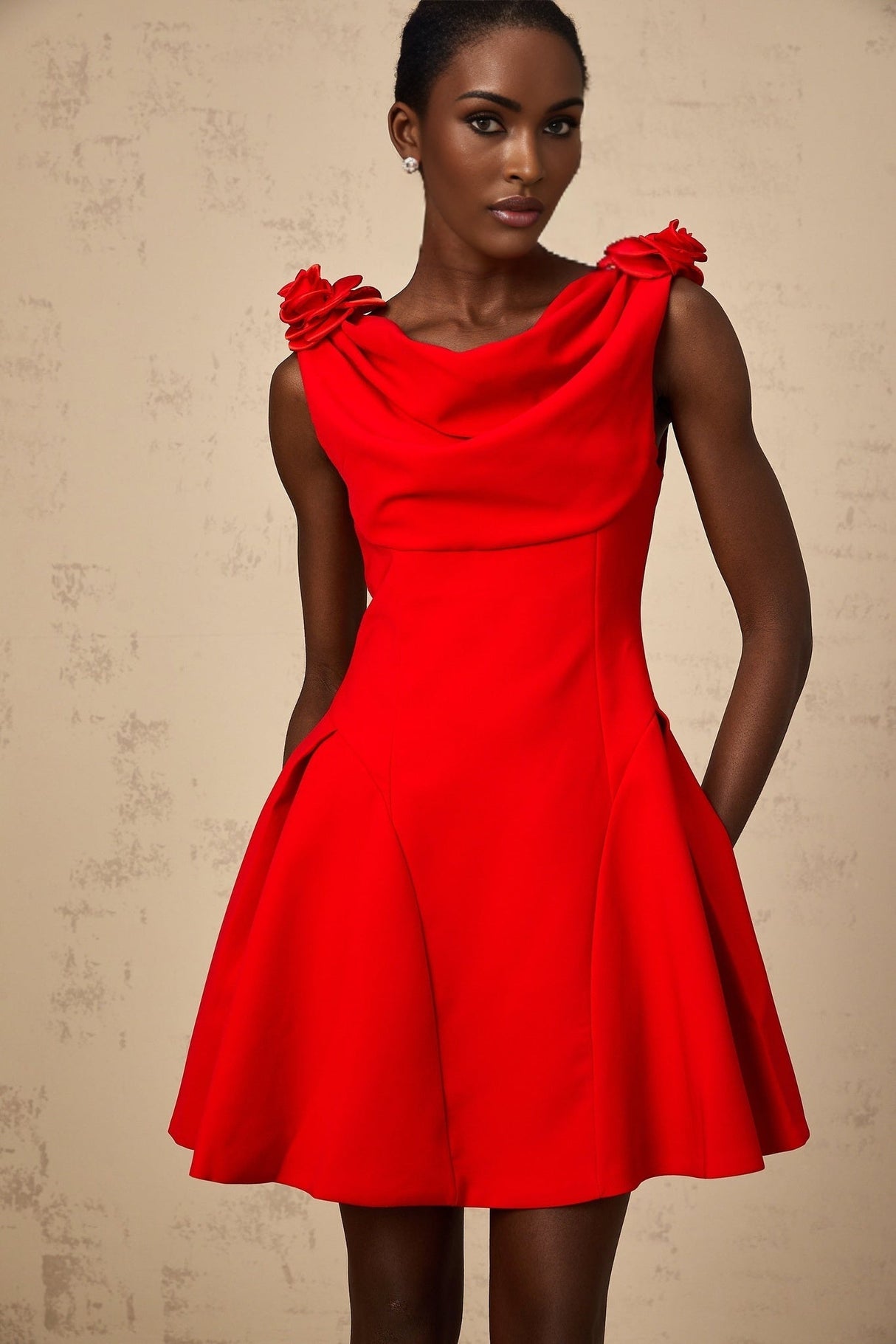 A woman wearing a bright red sleeveless mini dress with faux flower embellishments standing in a neutral background