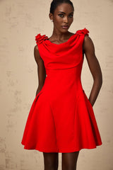 A woman wearing a bright red sleeveless mini dress with faux flower embellishments standing in a neutral background