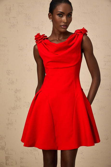 A woman wearing a bright red sleeveless mini dress with faux flower embellishments standing in a neutral background