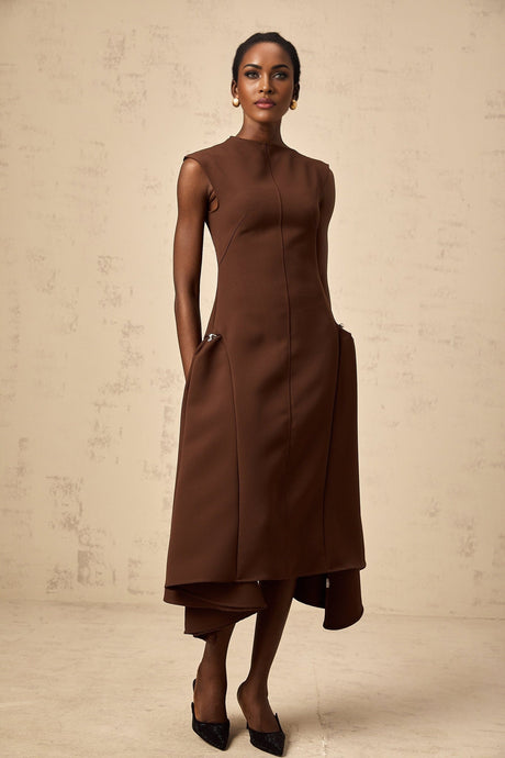 A woman wearing a brown asymmetric midi dress with a flowy skirt and one shoulder design