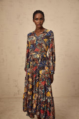 A woman wearing a brown bohemian style midi dress with shirring detail and flowing fabric standing in a casual pose